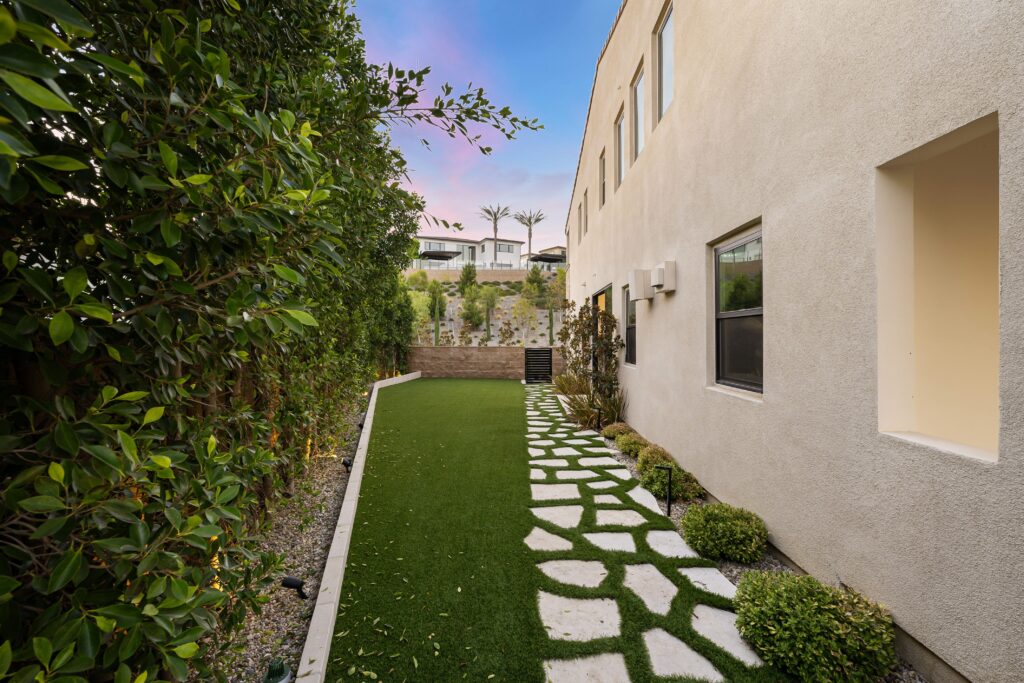 Modern backyard with artificial grass and stone path at sunset.
